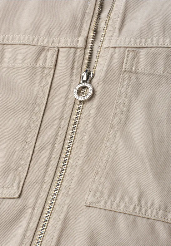 Close-up van een beige jack met rits en opgestikte zakken.