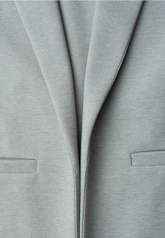 Nahaufnahme eines hellgrauen Blazers mit leichten Falten und dezenten Taschen.