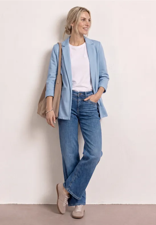 Femme en blazer bleu clair, t-shirt blanc, jean, baskets et sac épaule.