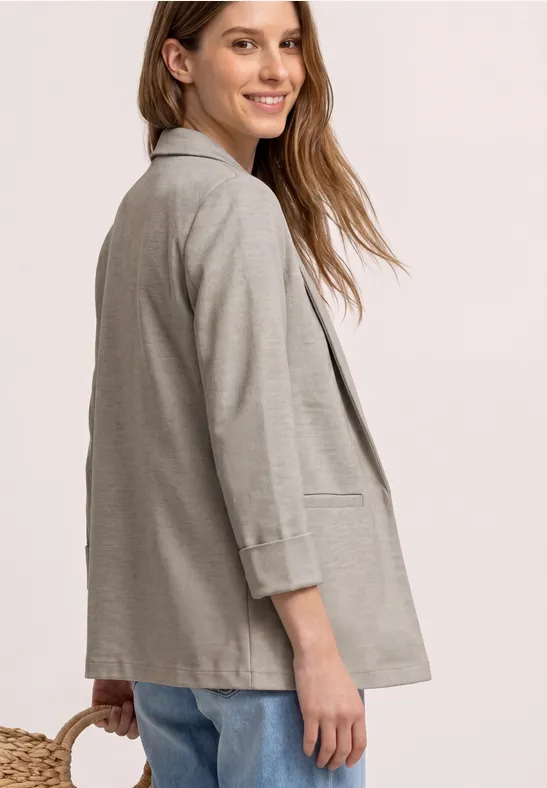 Femme en veste grise décontractée, vue de profil sur fond clair.