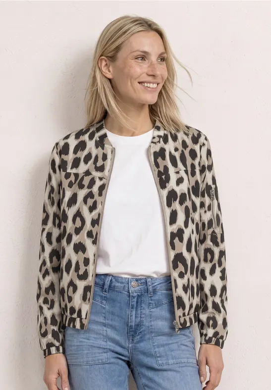 Femme blonde porte une veste bomber léopard, t-shirt blanc et jean bleu sur fond clair.