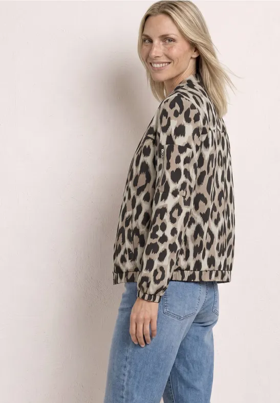 Femme de profil portant une veste léopard et un jean bleu sur fond clair.