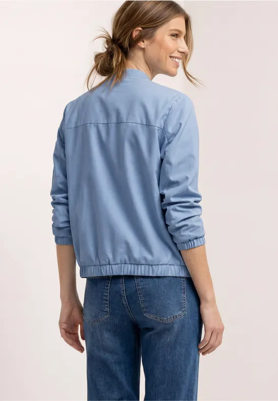 Vrouw van achteren in een blauwe bomberjas en spijkerbroek.