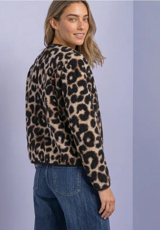 Frau mit blondem Haar trägt leopardenmuster Pullover und Jeans, blickt lächelnd über die Schulter.