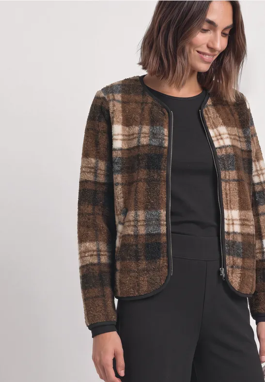 Frau mit dunkelbrauner Karo-Jacke über schwarzem Oberteil und Hose lächelt.