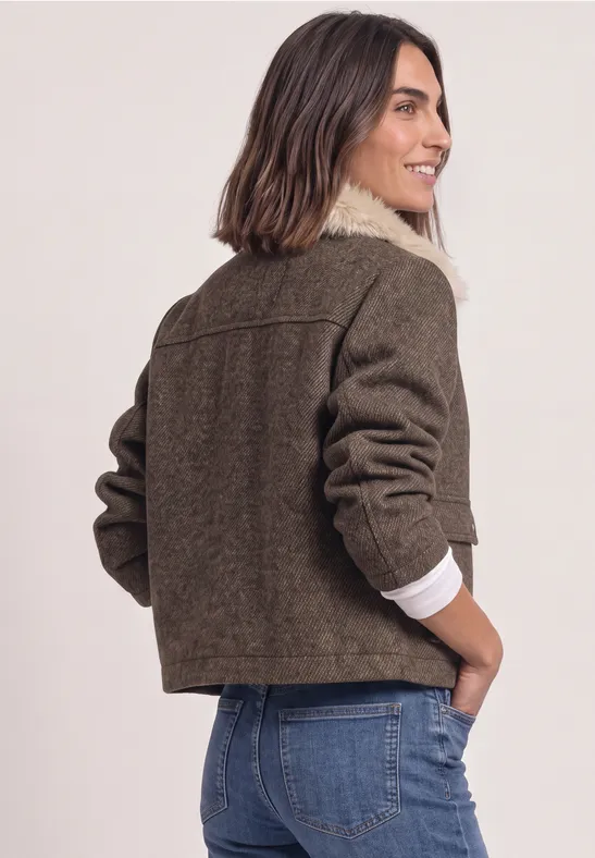 Frau von hinten in kurzen, braunen Wolljacke mit weißem Teddykragen und blauen Jeans.