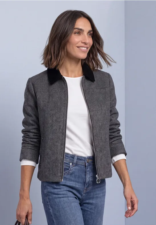 Lächelnde Frau im grau-schwarzen Blazer, weißem Shirt und blauen Jeans, die vorbeigeht.