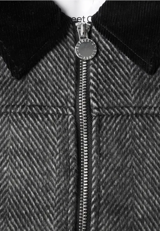 Nahaufnahme einer grauen Fischgrät-Jacke mit schwarzem Kragen und Reißverschluss.