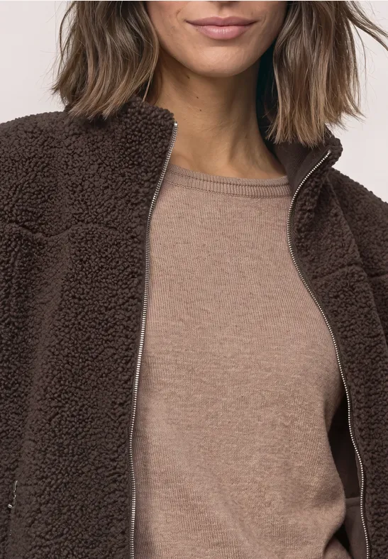 Osoba ma na sobie brązową kurtkę teddy fleece na beżowym topie.