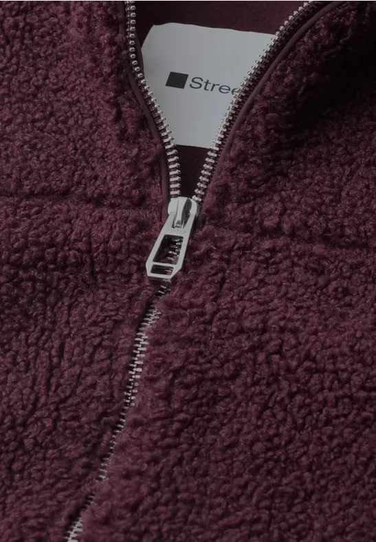 Zbliżenie bordowej polarkowej bluzy z metalowym zamkiem i widoczną metką.