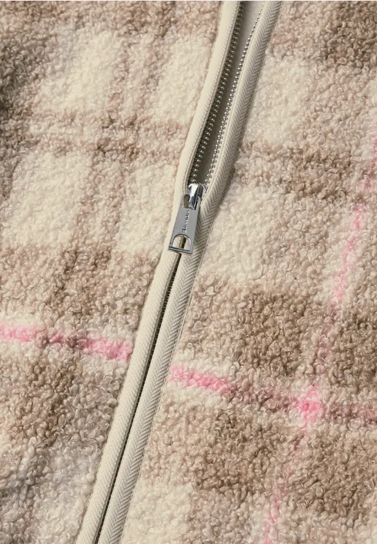 Nahaufnahme eines graubeigen Reißverschlusses auf kariertem Wollstoff in Braun mit dezenten rosa Streifen.
