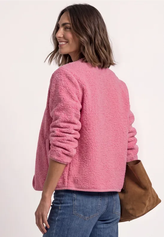 Frau trägt pinke Teddyjacke, blickt über die Schulter, kombiniert mit Jeans und einer braunen Tasche.