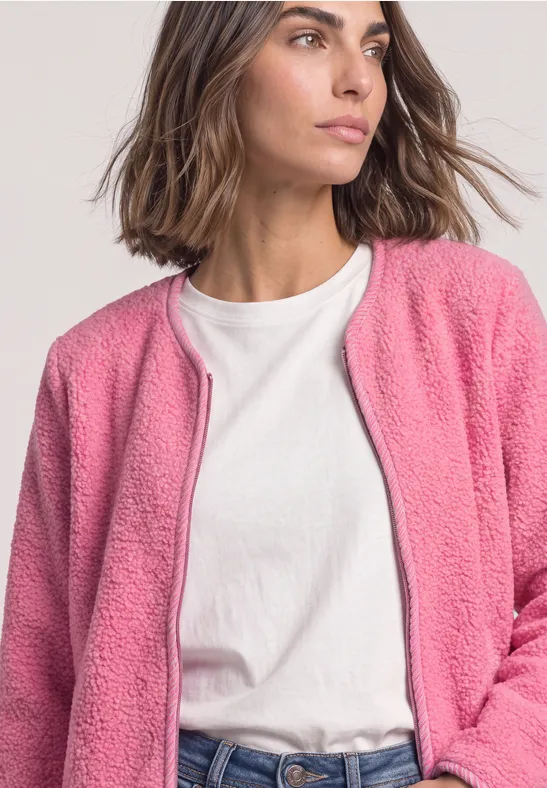 Eine Frau in weißem T-Shirt und pinker, flauschiger Fleecejacke.