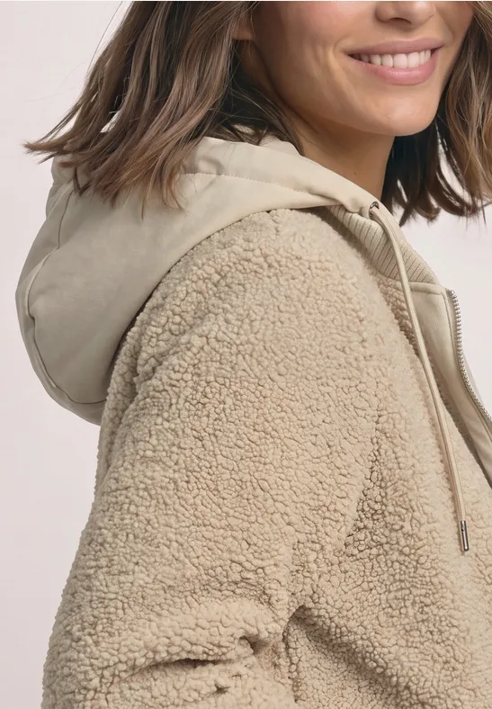 Nahaufnahme einer Frau in einer beigen Teddy-Fleecejacke mit Kapuze.