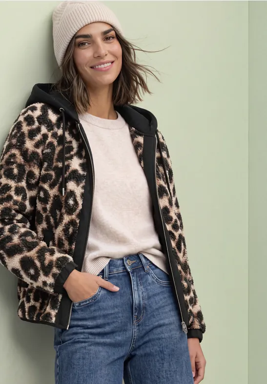 Frau in Jeans, Beanie und Leoparden-Fleecejacke lächelt entspannt.