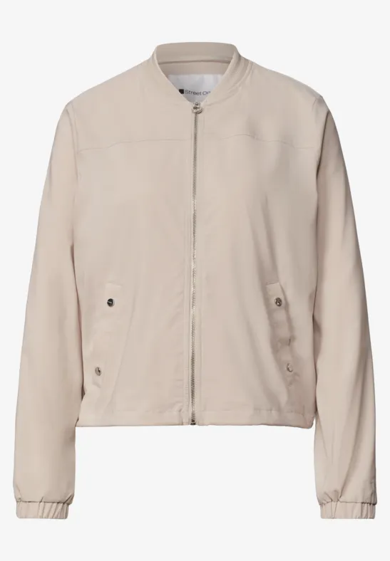 Helles beiges Bomberjacke mit Reißverschluss, seitlichen Taschen und langen Ärmeln.