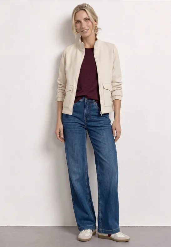 Femme en bomber beige, haut bordeaux, jean large taille haute et baskets blanches.