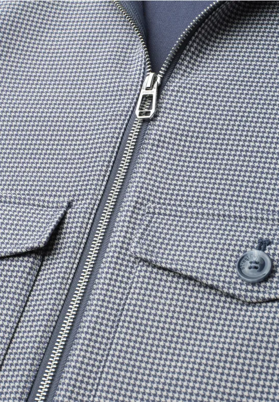 Gros plan d'une veste gris clair à motif micro-carreaux bleus, fermeture éclair et poche à bouton