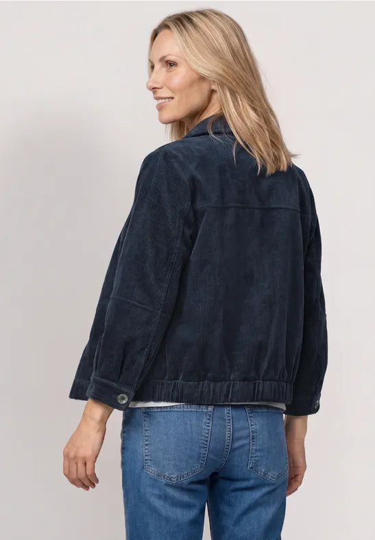 Rückansicht einer Frau mit dunkler Jacke und Jeans vor weißem Hintergrund.