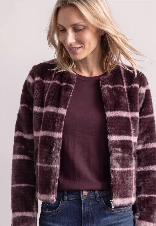 Frau mit blonden Haaren trägt braun-violette kariierte, pelzige Jacke und burgunderfarbenen Pullover.