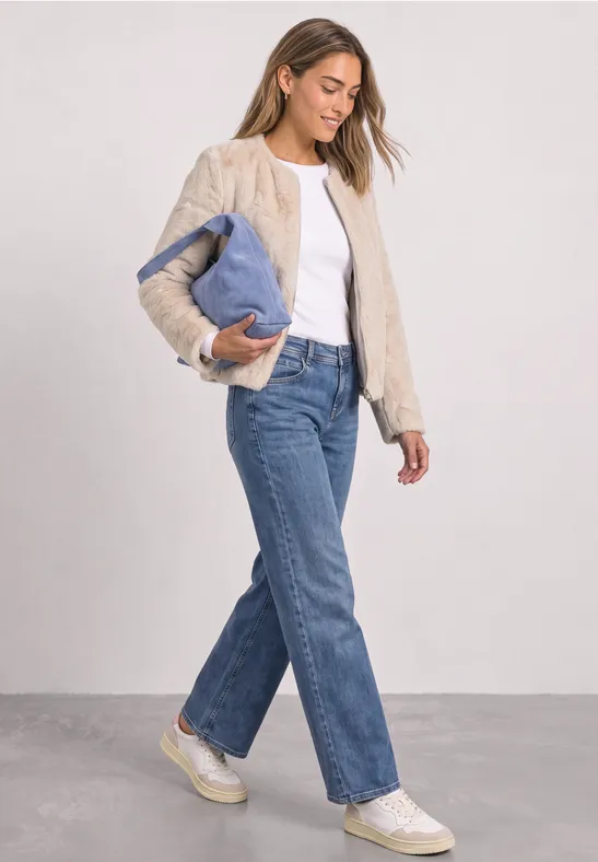 Frau in Jeans, weißem Shirt und beiger Weste trägt eine Jacke und läuft.