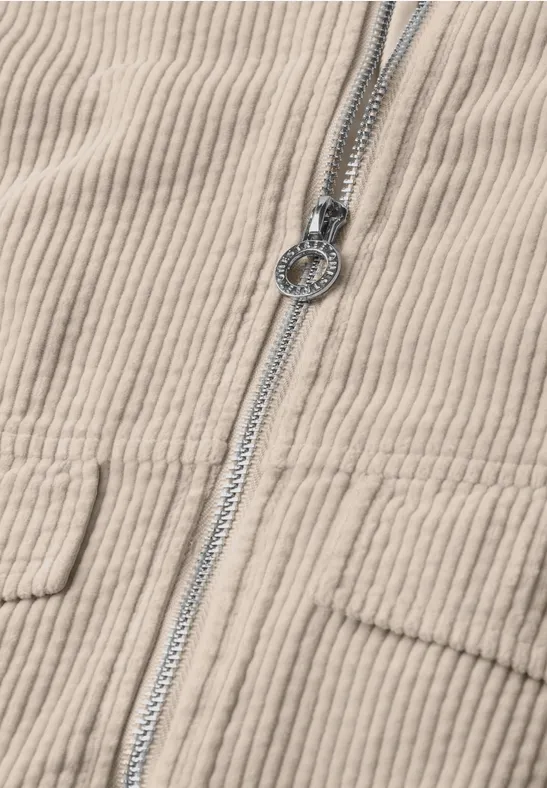 Beige Cordjacke mit sichtbarem Reißverschluss und rundem Metall-Zippergriff.