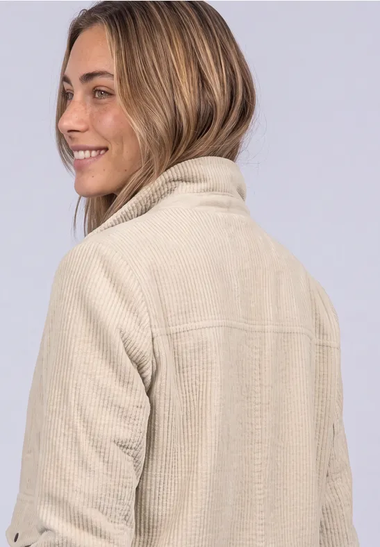 Eine Frau in beiger Cordjacke schaut über die Schulter und lächelt.