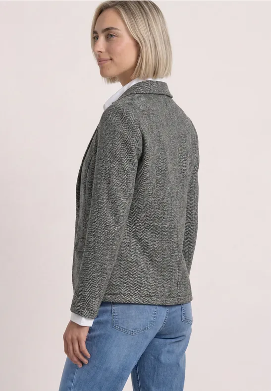 Seitlich zu sehen: Frau in grauem Blazer, weißer Bluse und blauen Jeans.