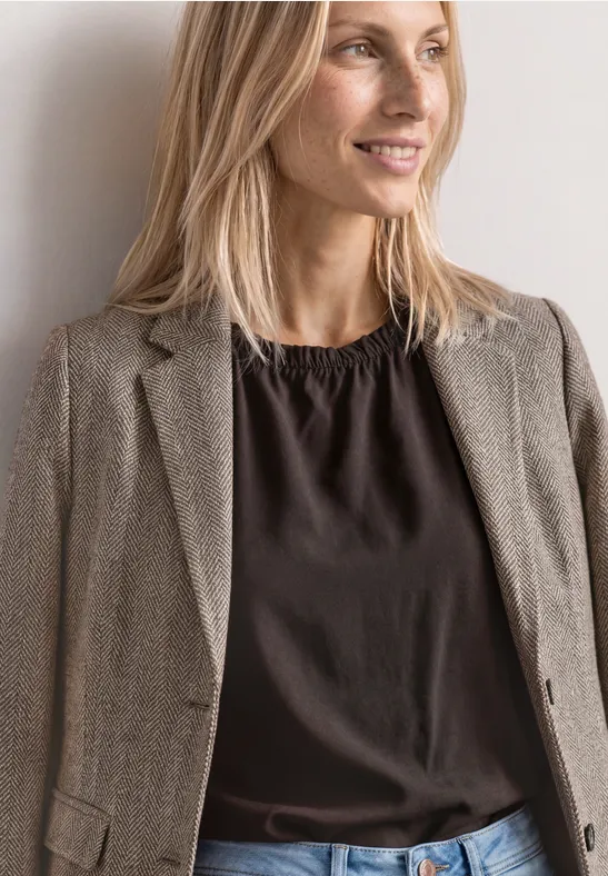 Uśmiechnięta blondynka w szarej marynarce i ciemnej bluzce na neutralnym tle.
