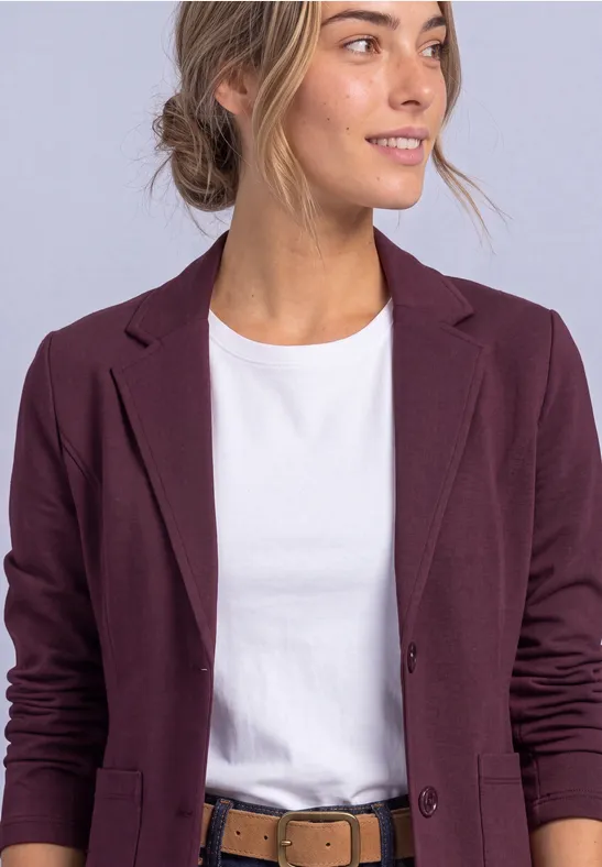 Vrouw met wit T-shirt en donkerpaarse blazer, kijkt iets naar rechts.