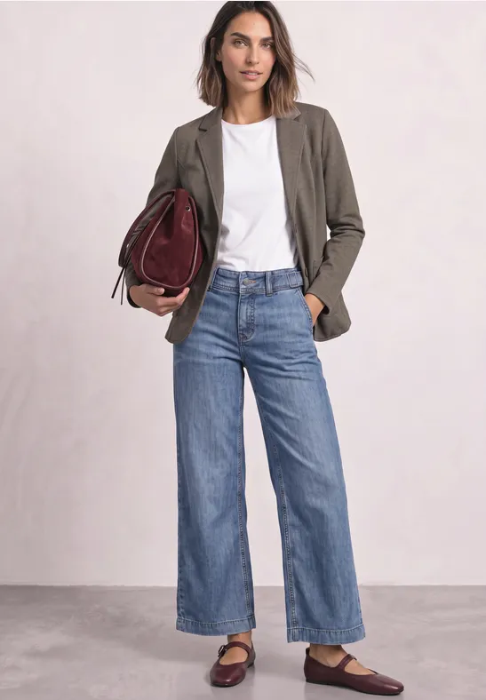 Frau in weißem T-Shirt, olivgrünem Blazer und weitem Jeans, mit weinroter Handtasche und Loafers.