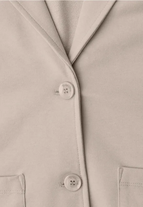 Beige Jacke mit Reverskragen, zwei Knöpfen und zwei aufgesetzten Taschen.