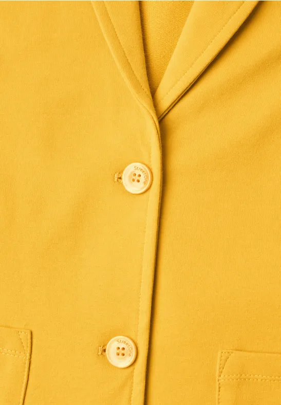 Nahaufnahme eines senfgelben Blazers mit zwei Knöpfen, Reverskragen und Taschen.
