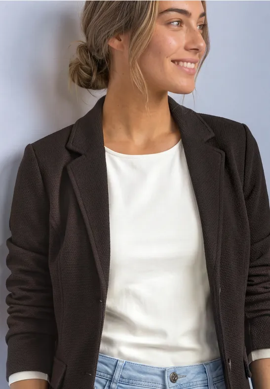 Une femme en blazer noir et haut blanc sourit de profil.