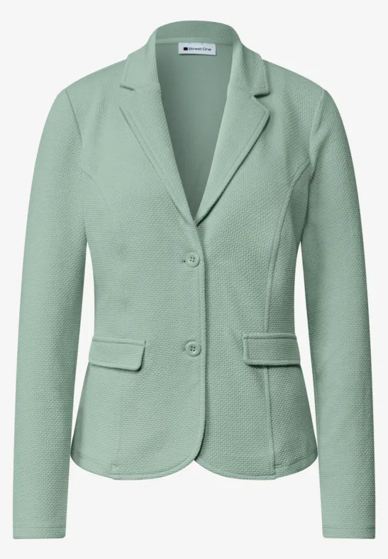 Grüner Damenblazer mit zwei Knöpfen, Reverskragen und aufgesetzten Taschen.