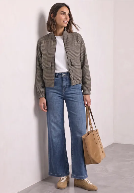 Femme en jeans larges taille haute, t-shirt blanc, veste courte verte et sac marron