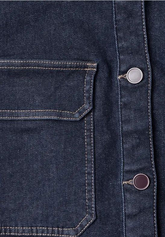 Gros plan d’une veste en jean foncé avec poche avant et boutons-pression métalliques.