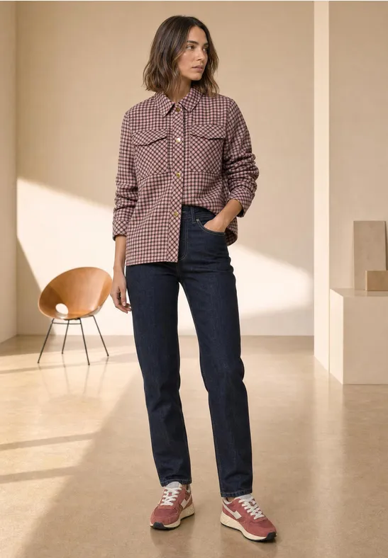Kobieta w kraciastej kurtce, ciemnych dżinsach i czerwonych sneakersach w minimalistycznej przestrzeni.