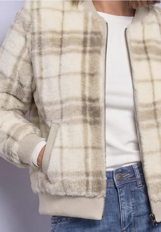 Buste d'une femme en veste crème à carreaux, T-shirt blanc et jean bleu.
