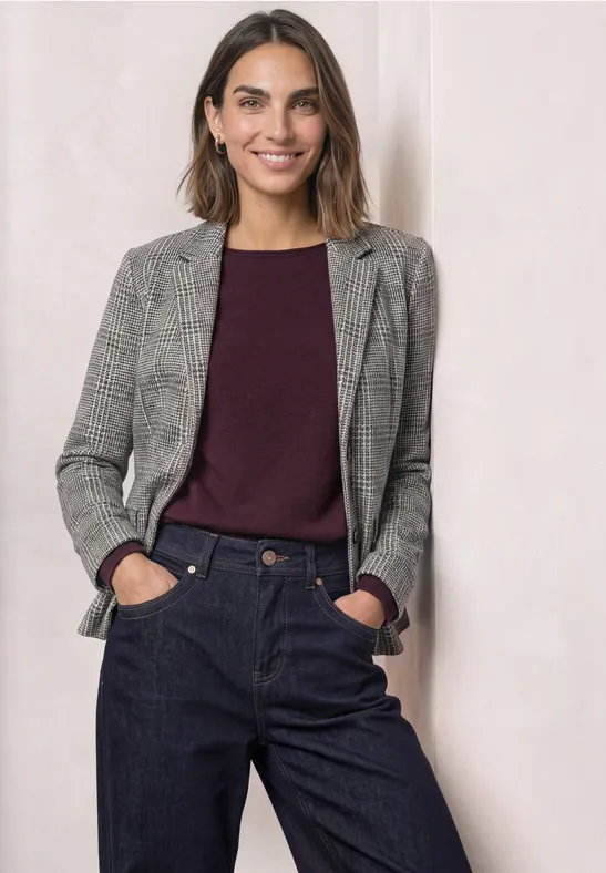 Eine Frau in grauem Blazer, bordeauxrotem Pullover und dunkler Hose.