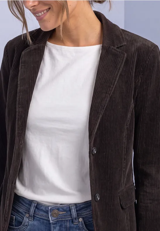 Persoon draagt een wit T-shirt, een bruine corduroy blazer en een jeans.