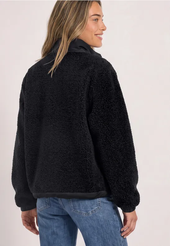 Frau trägt schwarzen, kuscheligen Teddy-Fleece-Pullover mit Stehkragen und halbem Reißverschluss.