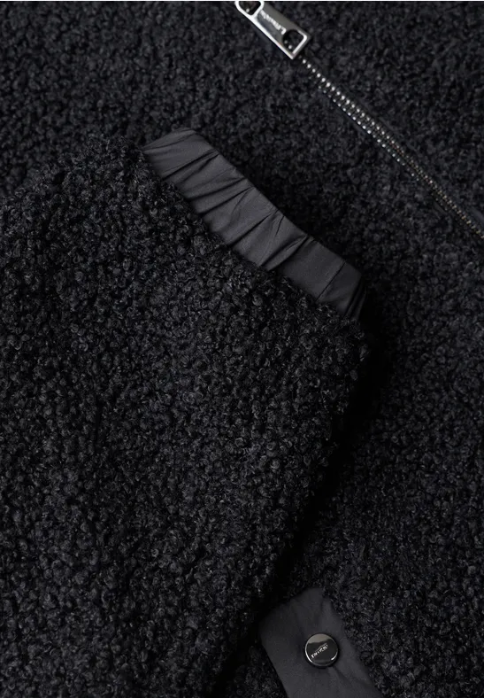Nahaufnahme eines schwarzen Teddy-Fleece-Kleidungsstücks mit Reißverschluss, Raffung und Knopf.