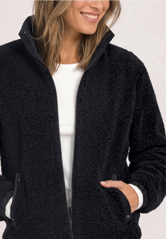 Eine Frau trägt eine flauschige schwarze Teddy-Fleecejacke mit Reißverschluss und lächelt.