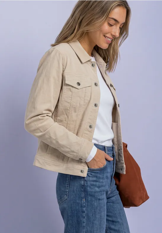 Seitliche Aufnahme einer lächelnden Frau mit beiger Jacke, weißem Shirt, Jeans und brauner Tasche.