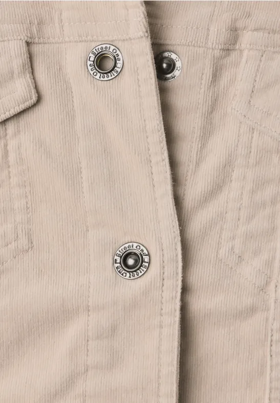 Nahaufnahme eines hellbeigen Cordjackenstoffs mit Metall-Druckknöpfen und aufgesetzter Tasche.