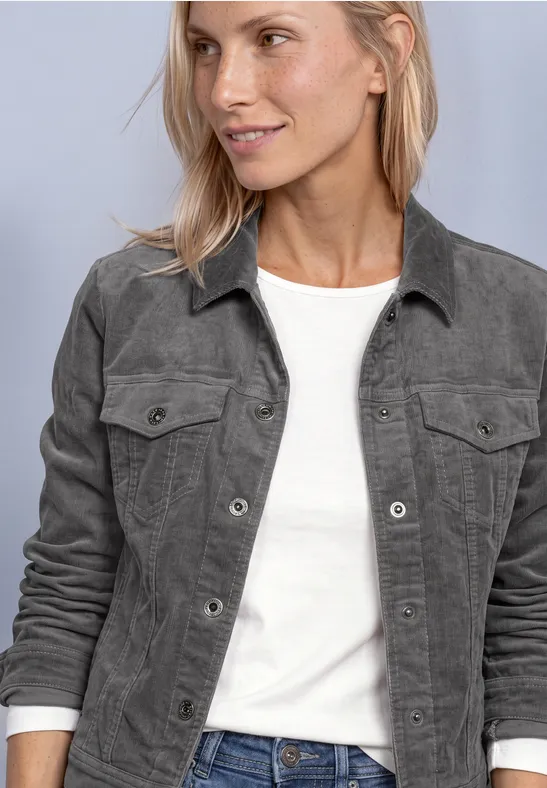 Une femme aux cheveux blonds porte un T-shirt blanc et une veste grise.