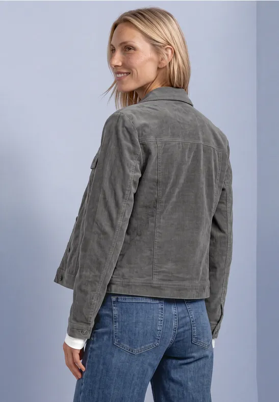 Femme en veste côtelée gris-vert et jean, regard par-dessus l'épaule