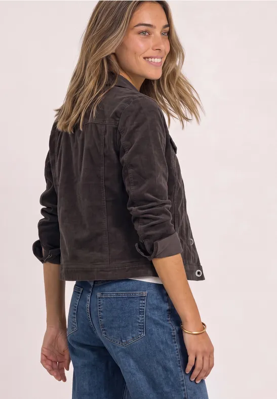 Femme souriante tourne la tête, porte veste brune courte et jean bleu