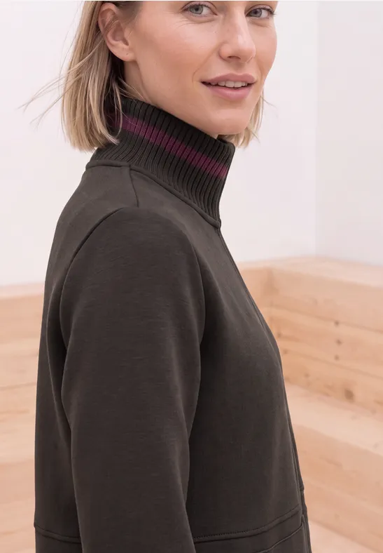 Blonde vrouw in donkere coltrui voor een lichte houten achtergrond.